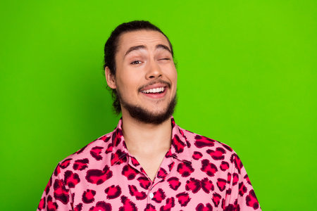 Young man wearing a stylish pink leopard print shirt posing against vibrant green background with cheerful expressionの写真素材