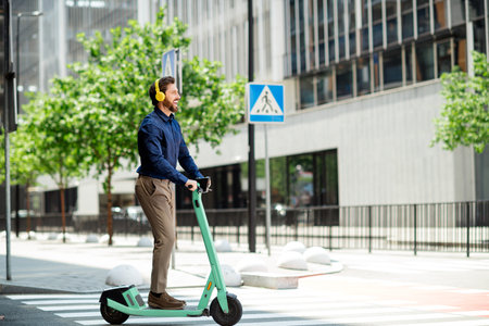 Young businessman on electric scooter listening to music through headphones riding in city during work commuteの写真素材