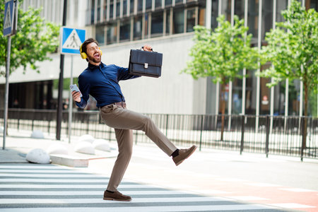 Joyful businessman enjoying music and dancing outdoors on a sunny day in the cityの写真素材