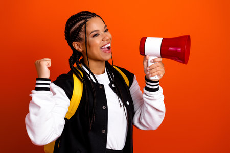 Energetic student celebrating achievement while holding a red megaphone against orange background in...
