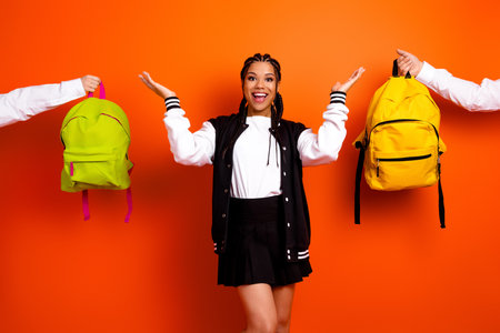 Young schoolgirl showcasing style with colorful backpacks on a vibrant orange background