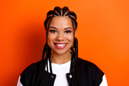 Portrait of a smiling young woman with braided hair wearing casual attire against an orange...