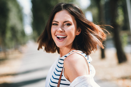 Young woman enjoying a sunny day outdoors with a joyful smile in a casual striped shirtの写真素材