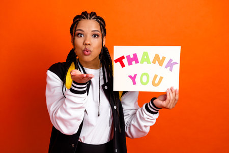 Smiling Teen Girl Sharing Appreciation With Thank You Sign Gesturing Positivity on Orange Backgroundの写真素材