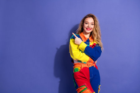 Young woman in vibrant multicolor denim outfit gesturing confidently against a bold violet...