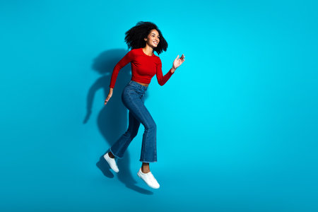 Dynamic photo of a young woman in vibrant casual red and blue attire joyfully jumping on a bright...