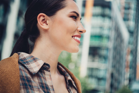 Portrait of a young woman smiling outdoors wearing casual plaid shirt in an urban city environment...
