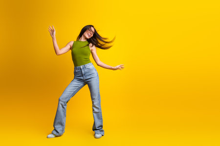 Cheerful woman posing in stylish denim jeans and khaki top against a vibrant yellow background, embracing summer vibesの写真素材