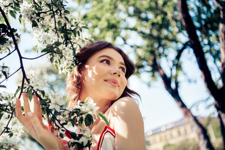 Young woman enjoying a sunny day outdoors surrounded by blooming flowers, radiating happiness and tranquility in a lush park settingの写真素材