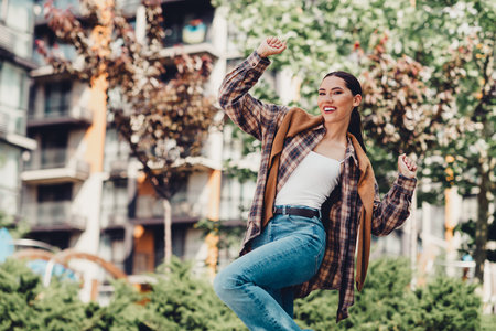 Young woman enjoying a sunny day outdoors in stylish casual outfit with vibrant energy surrounded by urban cityscapeの写真素材