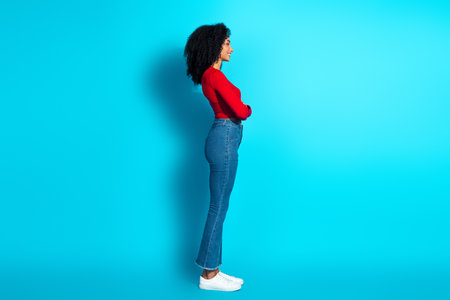 Portrait of a stylish young woman in a red top and jeans against a vibrant blue backgroundの写真素材