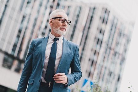 Confident senior business professional in formalwear outdoors against an urban office building background on a sunny dayの写真素材