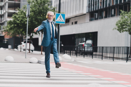 Confident businessman walking outdoors in a city street, wearing formal suit and headphones while smiling and enjoying the dayの写真素材