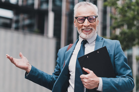 Mature businessman in formal suit outdoors holding clipboard in urban environmentの写真素材