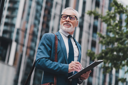 Successful senior businessman wearing a modern suit outdoors, holding a clipboard, exuding professionalismの写真素材