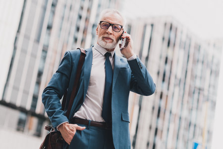 Mature businessman in a blue suit talking on a smartphone outdoors in an urban city environment while showcasing confidenceの写真素材