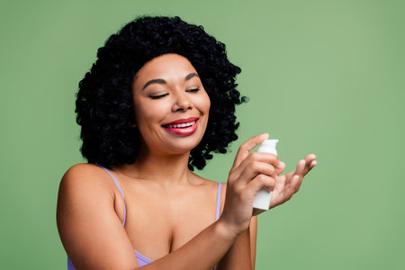 Attractive woman with natural curls applying skincare product, promoting body positivity and self-care with a radiant smileの写真素材