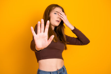 Young woman with brown hair in casual outfit posing against a vibrant yellow background with expressive hand actionの写真素材