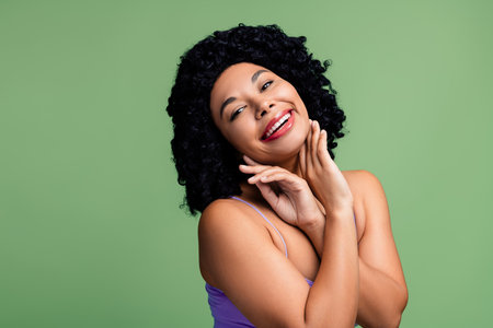 Portrait of a vibrant woman with natural curly hair against a bright green background radiating...