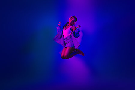Young woman in a vibrant neon environment, dancing joyfully, showcasing casual fashion and an...