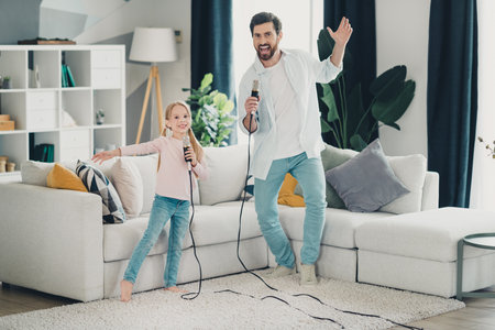 Father and daughter singing karaoke together at home, enjoying family time and bonding with laughter and joy in a cozy living roomの写真素材