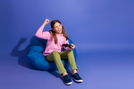 Energetic young girl enjoying a gaming session while relaxing on a beanbag chair against a vibrant...