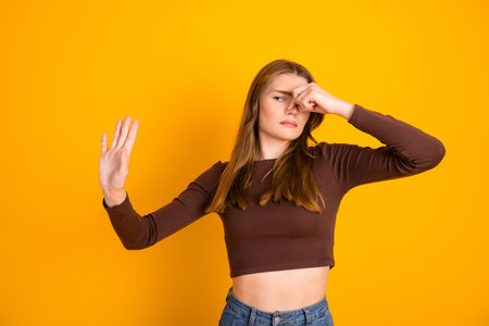Young woman pinching her nose while expressing discomfort against a vibrant yellow backgroundの写真素材