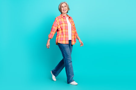 Elderly woman in casual outfit walking confidently on teal background, showcasing happiness, health, and an active lifestyleの写真素材