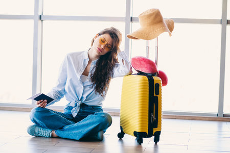 Passenger woman at airport resting with suitcase and passport during trip preparation for new travel destinationの写真素材