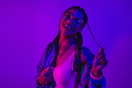 Young woman enjoying vibrant neon lighting with a cheerful expression and stylish denim clothing in...