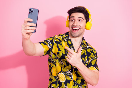 Cheerful Young Man Wearing Yellow Headphones Takes Selfie on Phone Against Vibrant Pink Background