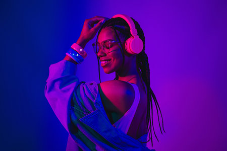 Vibrant neon portrait of a young woman wearing headphones enjoying music with a stylish denim jacket...