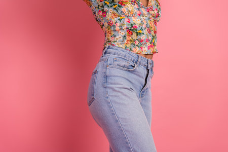 Trendy young woman in floral blouse and jeans with pink background creating a vibrant and stylish fashion expressionの写真素材