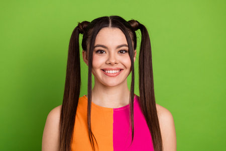Charming young woman with trendy ponytail hairstyle smiling brightly against a green background in vibrant fashion attireの写真素材