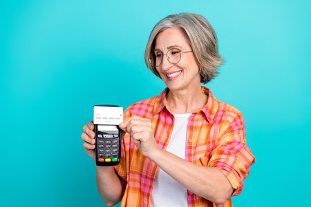 Elderly Woman Holding a Card Reader Against Vibrant Teal Background Creating a Friendly and Cheerful Gestureの写真素材