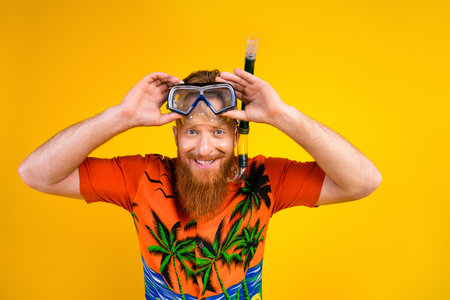 Happy young man with snorkeling gear and tropical printed shirt against vibrant yellow background showing excitementの写真素材