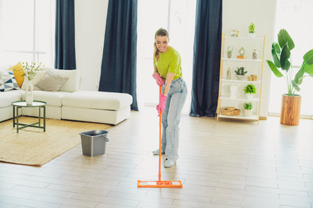 Young woman enjoying spring cleaning while mopping the living room floor in a stylish and comfortable apartmentの写真素材