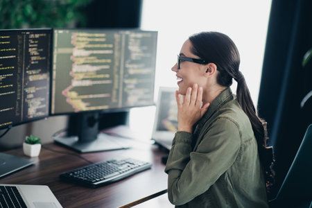 Charming woman programmer in a casual workplace surrounded by monitors coding and working on software developmentの写真素材