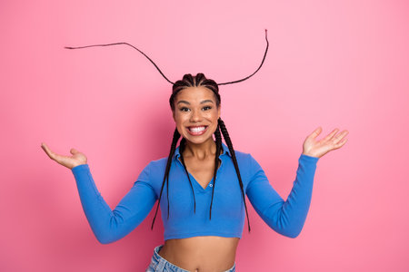 Joyful young woman in stylish blue top with braided hair posing against vibrant pink studio backgroundの写真素材