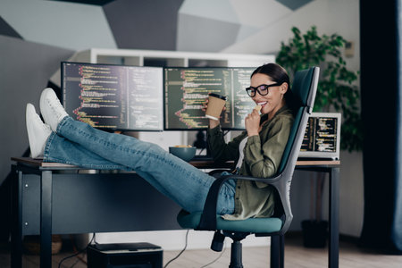 Qualified specialist enjoying coffee in a relaxed workspace with computers while working remotely on coding projectsの写真素材