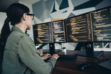 Female programmer coding at her desk with dual monitors in a modern workspace setting