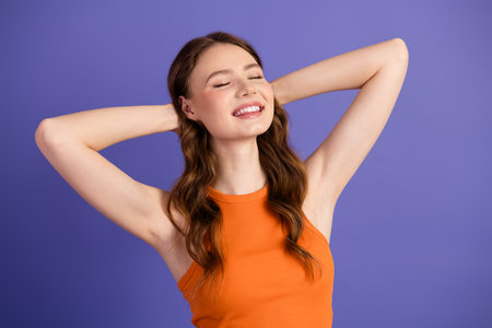 Carefree, showcasing her bright smile while wearing a vibrant orange top against a purple backgroundの写真素材