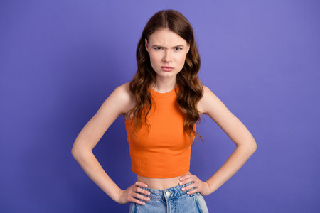 Young woman in stylish orange top expressing intense emotions against a violet background