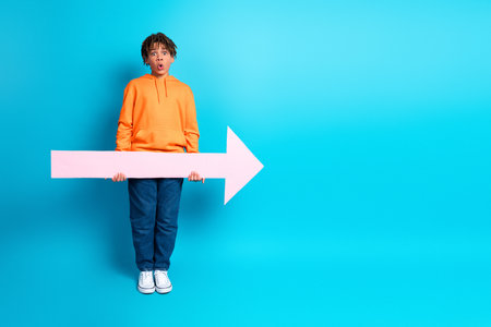 Young boy holding a pink arrow on a bright blue background showcasing an expressive and cheerful appearanceの写真素材