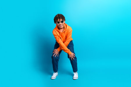 Energetic young boy in an orange hoodie and jeans posing dynamically on a vibrant blue background, expressing joy and styleの写真素材