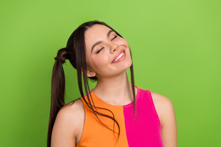 Charming young woman with a vibrant colorful top smiling gracefully against a bright green background radiating happinessの写真素材