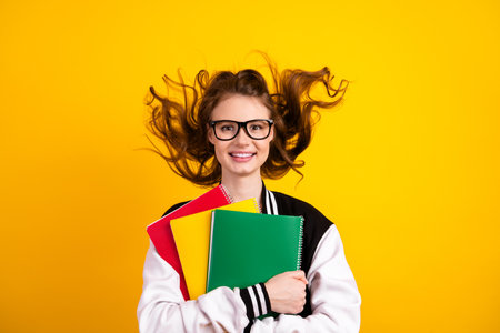 Cheerful young female student with book on yellow background embracing education and learning...