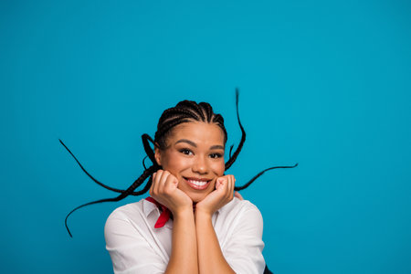 Cheerful young woman with braided hair poses joyfully against a vibrant blue background wearing casual fashionable attireの写真素材