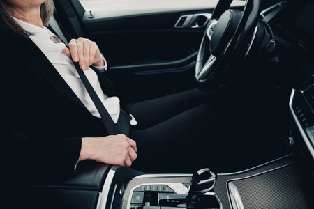 Elegant professional woman in formal attire fastening seatbelt inside a modern vehicle during commute in daylightの写真素材