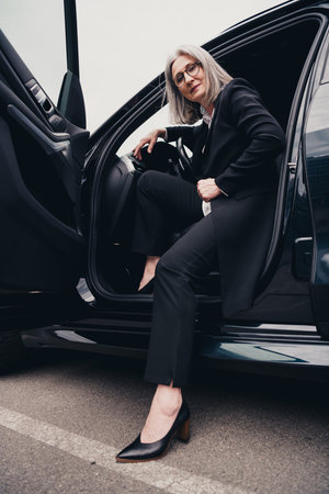Mature businesswoman in formalwear stepping out of a car during a workday in a city environmentの写真素材